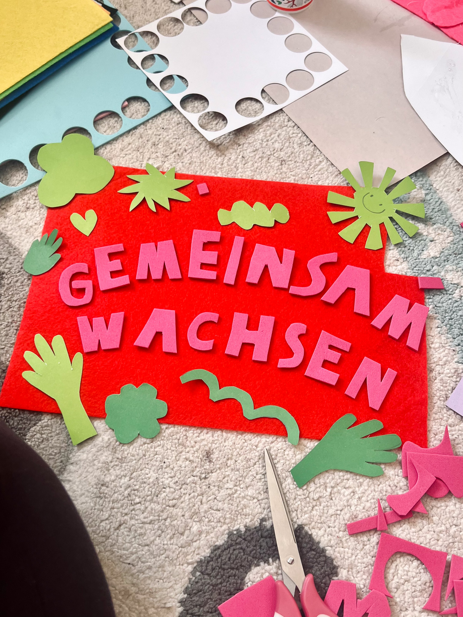 Colorful craft materials arranged on a surface, featuring the phrase 'Gemeinsam Wachsen' in playful letters.