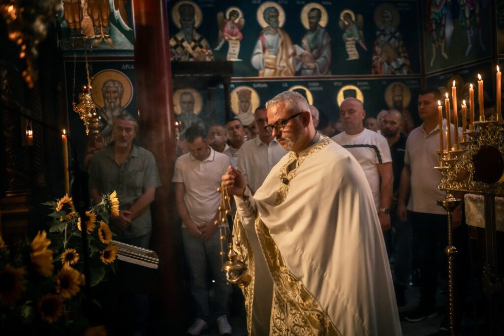 A priest conducts a religious ceremony in a church, surrounded by worshippers and illuminated candles.