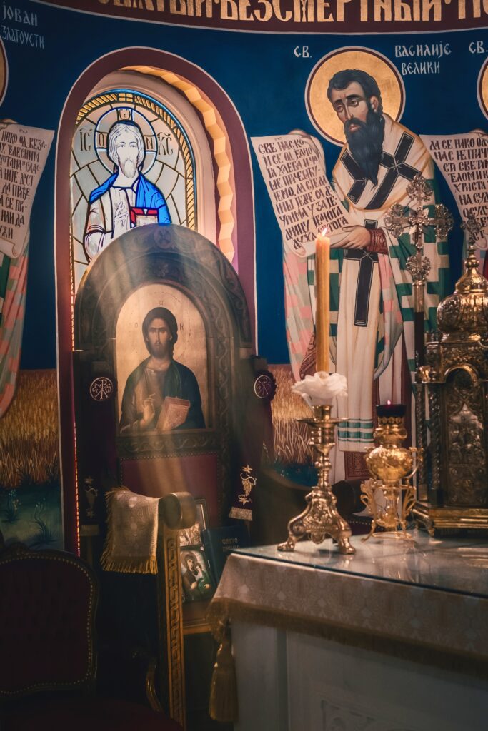 Interior of a church featuring religious icons, stained glass, and ornate altar decor illuminated by soft light.