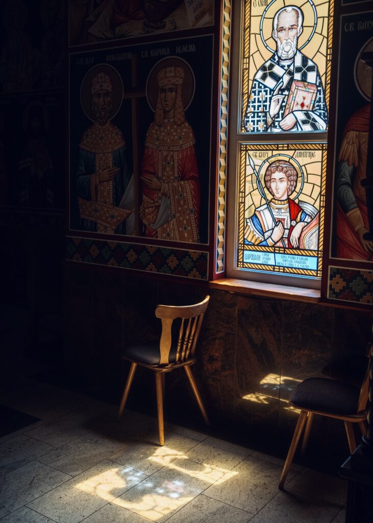 A wooden chair illuminated by sunlight near stained glass windows depicting religious figures in a serene interior.