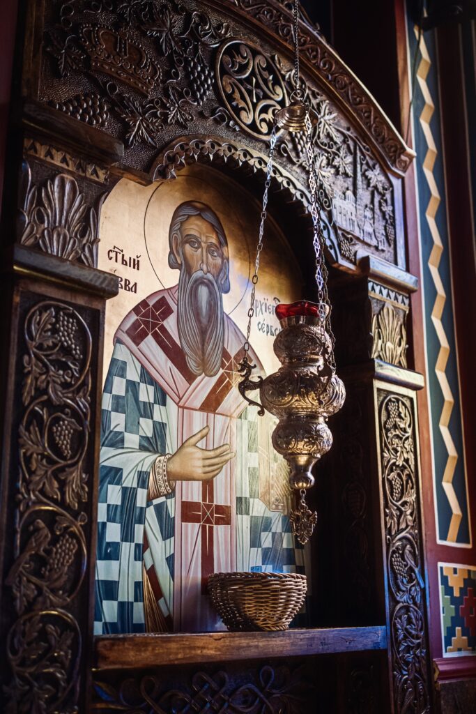 An ornate wooden altar featuring a religious icon of a saint, with intricate carvings and a hanging oil lamp.
