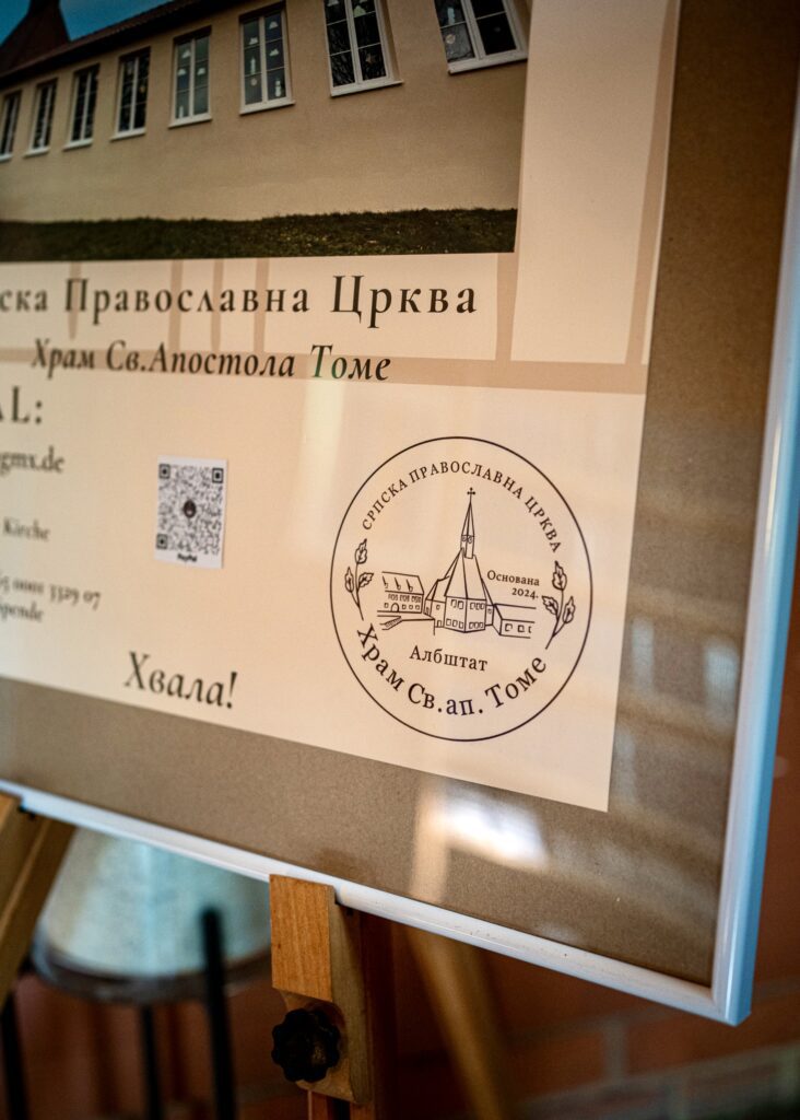 A framed informational poster for the Serbian Orthodox Church of Saint Thomas in Albstadt, featuring a building photo, logo, and QR code.