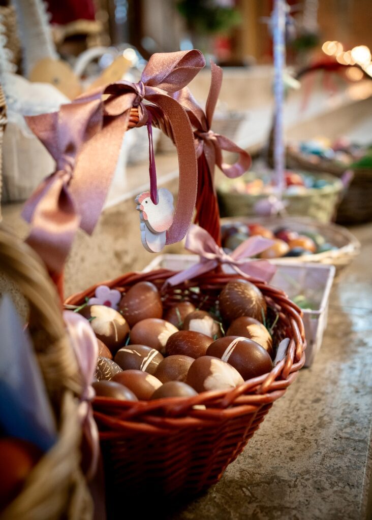 A decorative wicker basket filled with brown Easter eggs, adorned with a pink ribbon and a small wooden chicken ornament for holiday decor.