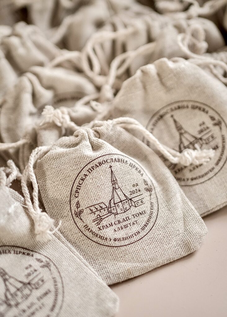 A collection of small, natural linen drawstring bags featuring a custom circular logo print for the Serbian Orthodox Church in Villingen.