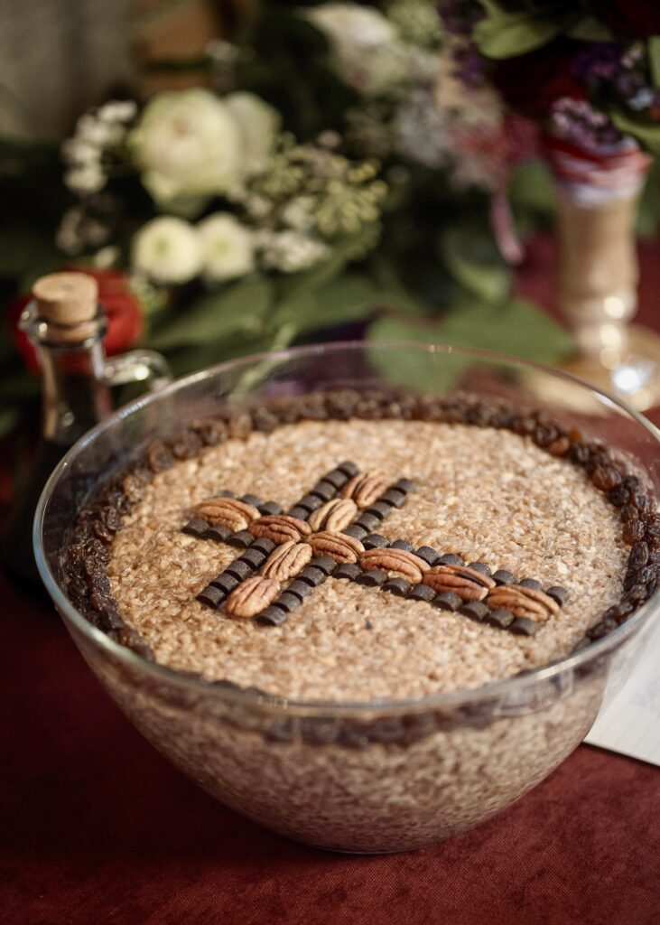 A glass bowl of traditional koliva wheat pudding decorated with a cross made of pecans and chocolate, served for a Greek memorial service.