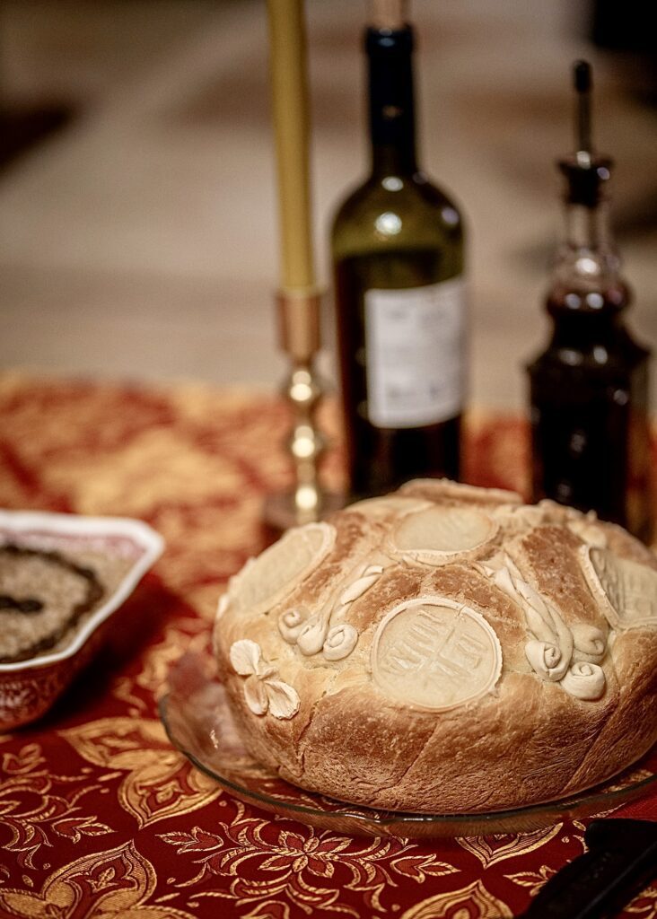 A traditional Orthodox Christian Slava bread decorated with religious symbols, placed on a table with wine and a candle for a celebration.
