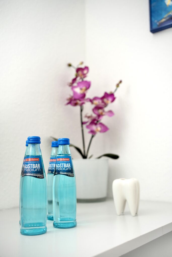 Three bottles of KASTBAR medium sparkling water on a white shelf with a decorative orchid and a tooth figurine.