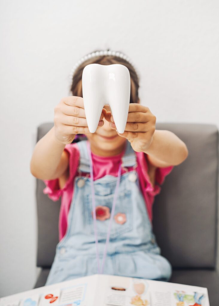 A child proudly holds a large white tooth model, promoting dental health awareness and education.