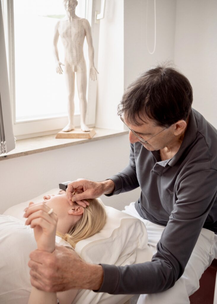 A practitioner performs a therapeutic treatment on a patient in a clinical setting, with an anatomical model in the background.