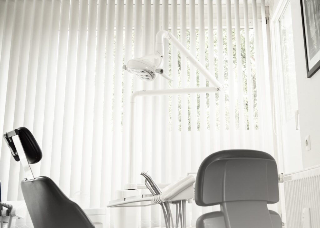 Modern dental clinic interior featuring dental chairs and bright natural light through vertical blinds.