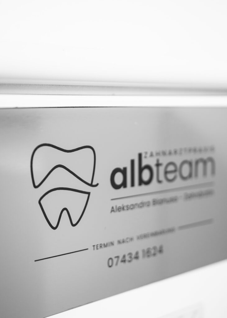 Close-up of a dental practice sign featuring the logo and contact information for albteam dental clinic.