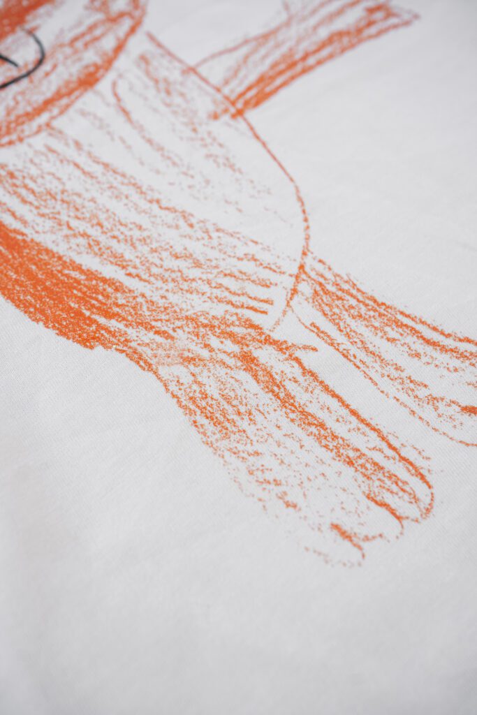 A close-up view of a white fabric featuring a vibrant orange crayon-style illustration of a bird, showcasing textured, hand-drawn artistic lines.